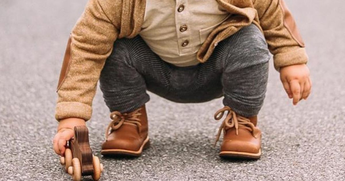 Close-up of toddler crouching with a wooden toy car — capturing a candid moment of joy, movement, and imagination.